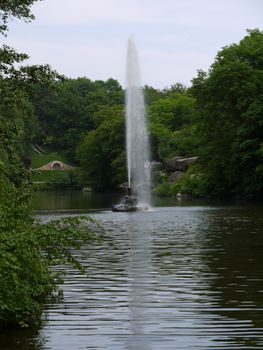 A huge fountain in the middle of the lake against the backdrop of beautiful manicured lawns and green trees
