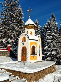 elegant chapel with a small dome with a cross on the background of snow-covered fir trees