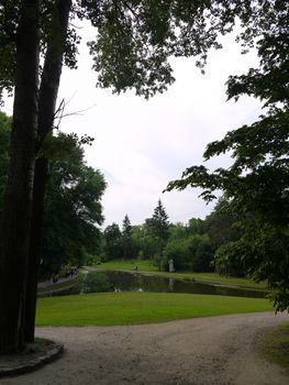 Magnificent view of the pond in the park with walking tourists on the beach with lawns with green grass next to it and trees growing around them.