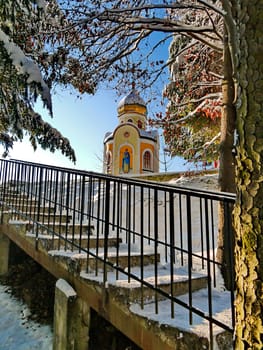 Snow-covered steps leading to a small church, against a backdrop of tall trees