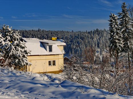 Scenic view of the snow-covered mountain range with a small comfortable wooden cottage