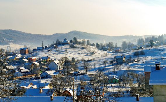 Rural settlement with small snow-covered houses, yards and a church on a hill