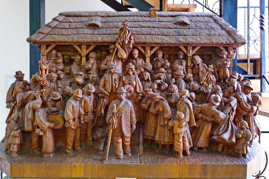 A composition of figures carved from a single piece of wood in national clothes standing near the house with a thatched roof.
