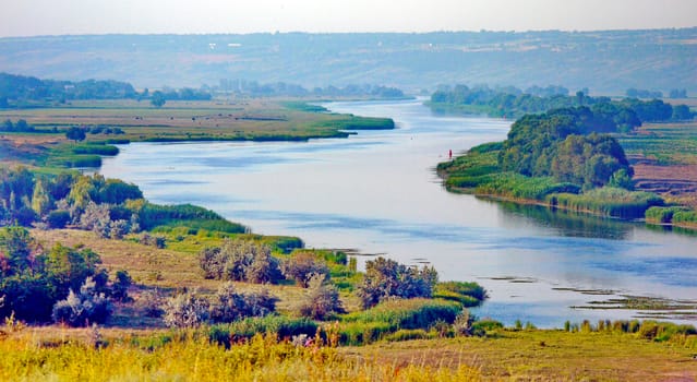Beautiful blue river bay on the background of wide fields and green forests