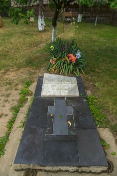 Memorial stone slab with cross on a background of green grass and flower beds with flowers