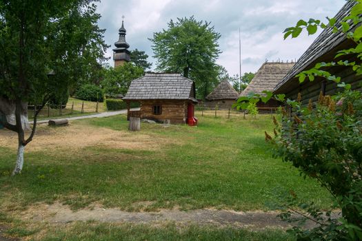 A small house with one window standing on a green grass in a historic park next to other objects of history.