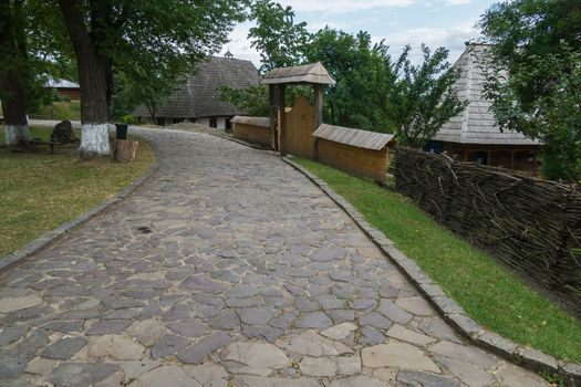 A stone alley along the fence leading to the wooden gate at the entrance to the decorative authentic Ukrainian city