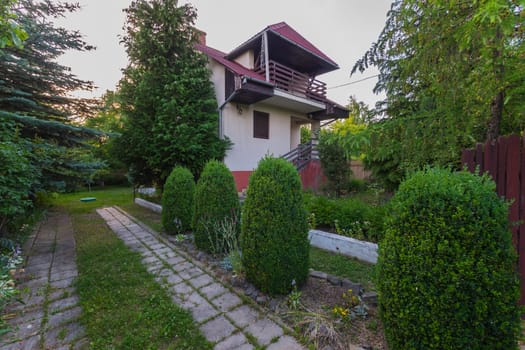 Two-storey white building with red socle and roof. Green bushes grow around it