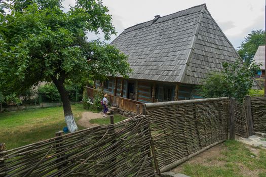 A tourist in the courtyard of an old house with a fence gate and wicket made from a vine with interest examines its architecture and arrangement.