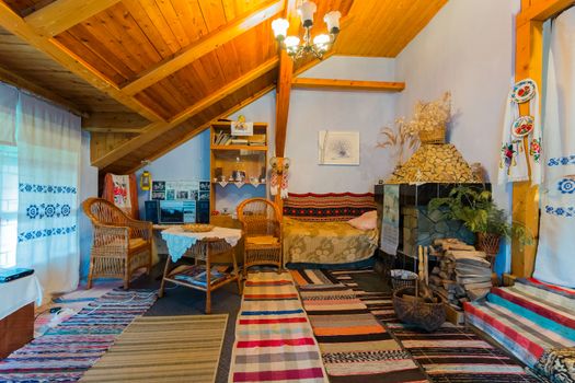 A room with a wooden ceiling with historical objects of everyday life. Woven tracks with patterns rugs furniture made from vines embroidered curtains painted with flowers plates.