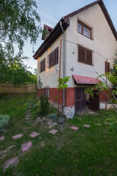 A country house with barred windows of green grass in the garden and a branch of fruit tree with ripe fruits.