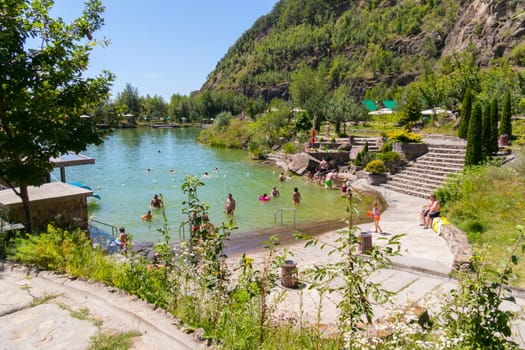 Holidaymakers on the beach near a transparent lake on the background of a large green rocky mountain