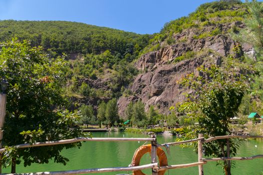 The lake at the foot of a rocky mountain is fenced with a wooden fence. Around a gazebo for rest