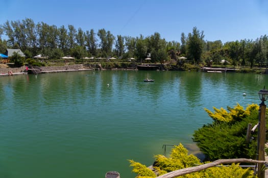 Green clear clear mountain lake in the background of a park zone with tents and umbrellas for tourists