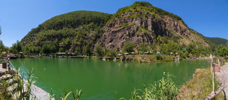 A beautiful view of the pond on a hot summer day is located at the foot of two mountains with stony slopes and overgrown with forest.