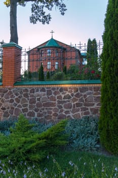 Church of red brick with a green roof behind a forged black high fence