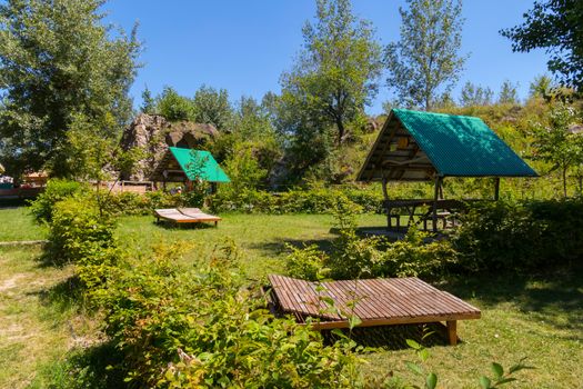 Comfortable wooden sun loungers and spacious gazebo with a green roof in the background of the park zone