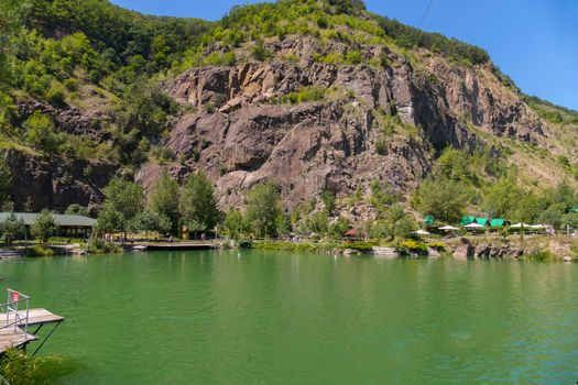 Recreation center with deep green lake on a background of rocky mountain and blue sky