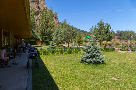 tourists at the tables in the shade under the peak of the building next to the green lawn