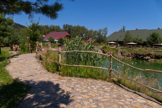 Recreation park with a large pond with paths lined with bricks stairs to the water cottages and resting people in the hot summer sun.