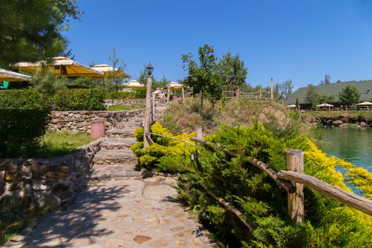 Stone steps with a wooden fence leading to a recreation area against the backdrop of a green lake and blue sky