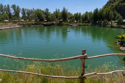 The tourist is floating on an inflatable mattress in the middle of a pond on a hot summer day fenced with a wooden hedge.