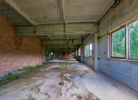 the building with a long concrete corridor overgrown with moss and windows has been thrown