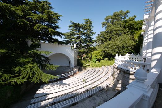 Summer amphitheater with several rows of benches, a spacious white balcony and a large stage