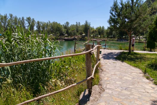 A road lined with a large stone with wooden rails, leading to a green transparent mountain lake