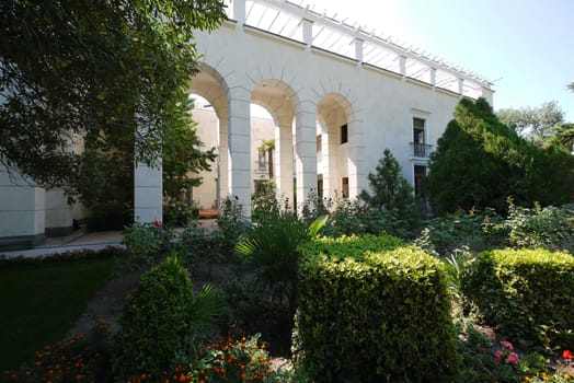 Beautiful white building with huge square pillars against the background of the green decorative zone