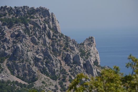 The gray, tall rock in the foreground covers the blue surface of sea water