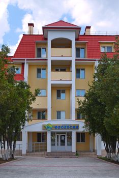 A cozy beige five-storey boarding house with large balconies and a red roof