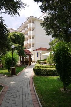 a tiled walkway running between green lawns to a gazebo for rest and a hotel