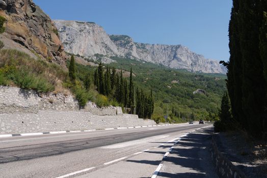 A large motorway on the background of high rocky mountains and green cypresses