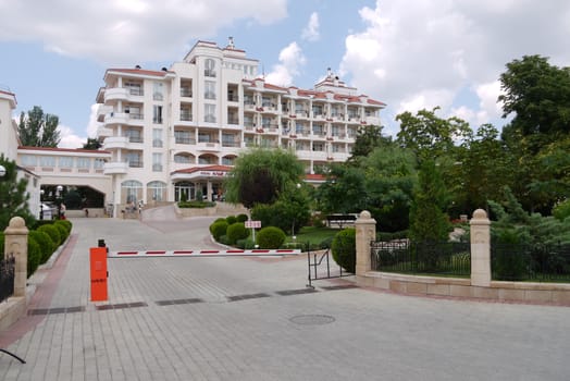 A beautiful multi-storey hotel with balconies with a picturesque green area next to it against a blue sky with clouds.