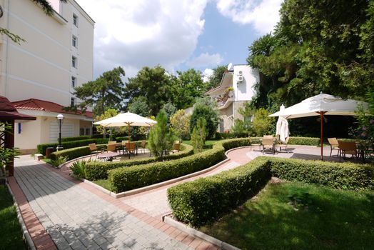 Rest zone with comfortable chairs, tables and umbrellas against the backdrop of the buildings of the sanatorium complex