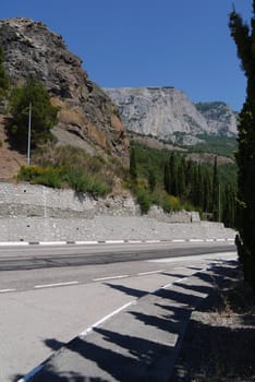 Highway with road markings going in the area with stony rocks and green trees growing on the slopes.