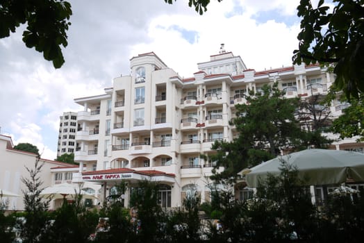 Beautiful views of the beautiful hotel with luxurious architecture and many balconies from under the trees with green foliage growing next to it.