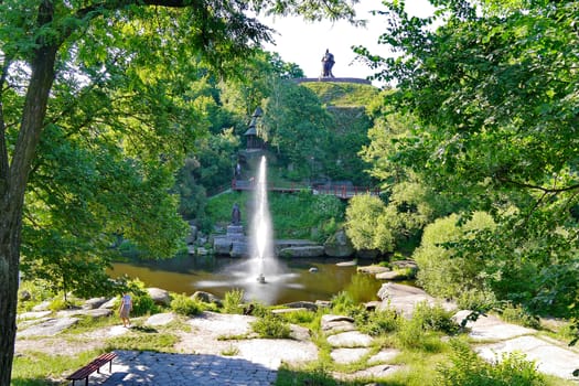 High deorativny fountain in the middle of the lake at the foot of a green hill with a pedestal