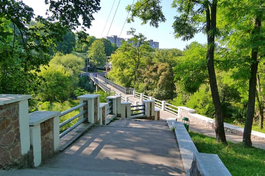 A wide staircase in a park with metal rails leading to high-rise buildings in the distance