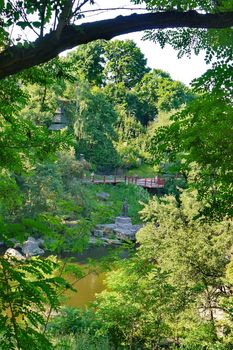 A bridge across the river in a green park with a stone statue on the shore