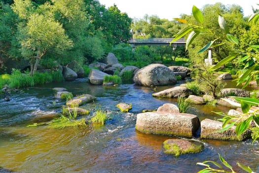 a pedestrian bridge over a river with large boulders in the city park