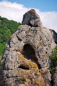 A gray rock with a red moss and a cave in it