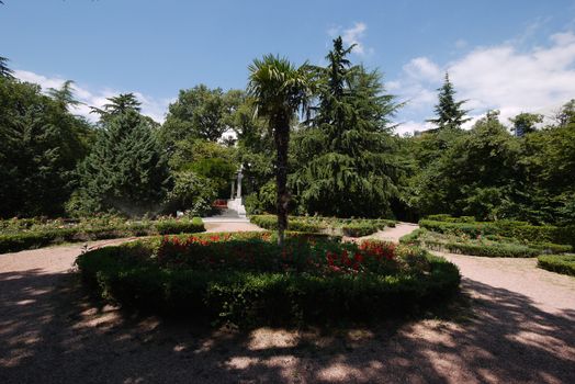 A flower bed with small ornamental flowers, green bushes and a high exotic palm tree