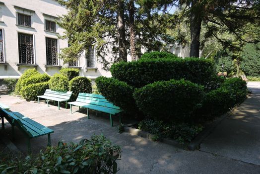 Figured flowerbeds and benches near a two-story gray building