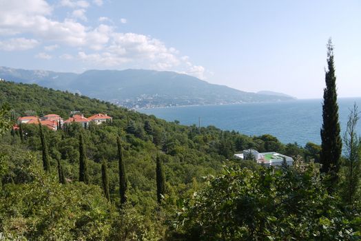 High green mountains with houses with a red roof against the backdrop of the endless blue sea