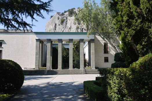 The park walking alley leading to the entrance with large square columns against the background of a high mountain