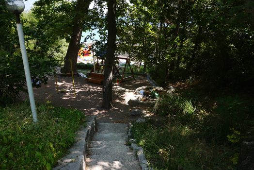 Steps leading down to the platform in the shade of the trees on which are located a bench for children's slide bar and a mini pond with a princess frog.