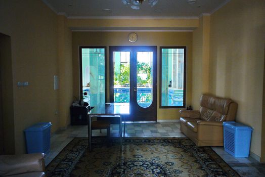 A spacious room with upholstered furniture and a large balcony. Over the exit to the balcony hang the wall clock