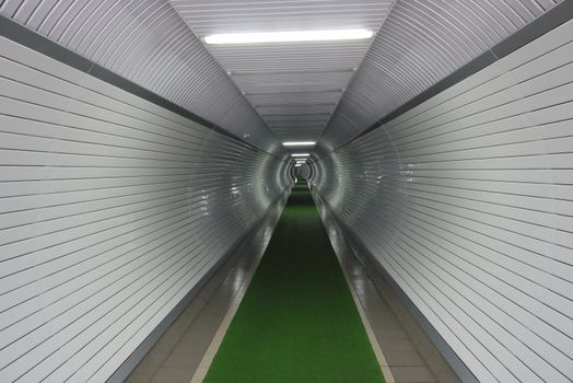 long white corridor in the basement with a green path on the tile, illuminated by daylight lamps